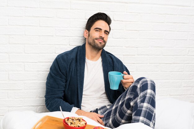 Homem na cama com roupão e tomando café da manhã