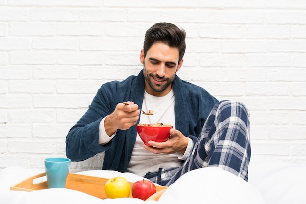 Homem na cama com roupão e tomando café da manhã