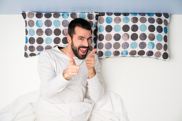 Homem na cama em vista superior, apontando para a frente e sorrindo