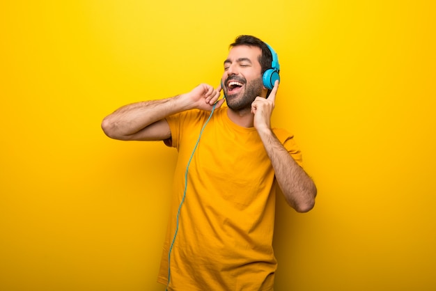 Homem na cor amarela vibrante isolada ouvindo música com fones de ouvido