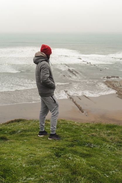 Homem na costa nublada olhando o mar na grama