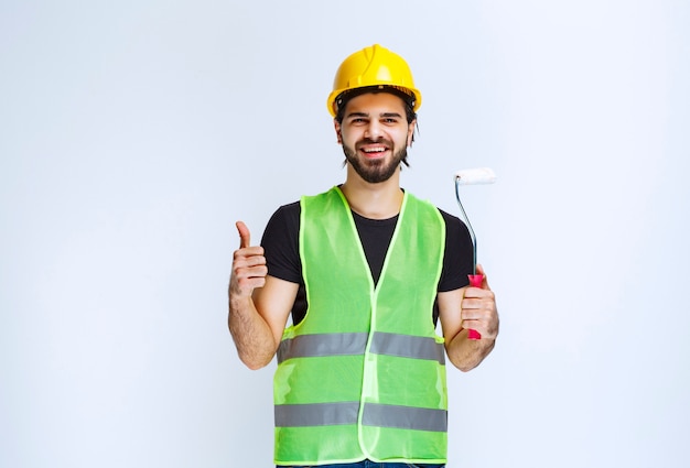 Homem na engrenagem amarela segurando um rolo de pintura e se sentindo satisfeito.