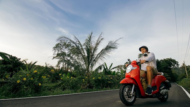 Homem na moto vermelha em roupas brancas dirige na trilha da floresta Um turista caucasiano de homens