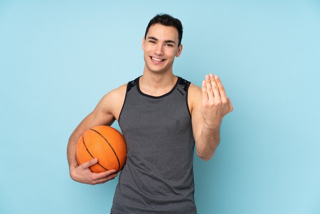 Homem na parede azul isolada, jogando basquete e fazendo o gesto que vem