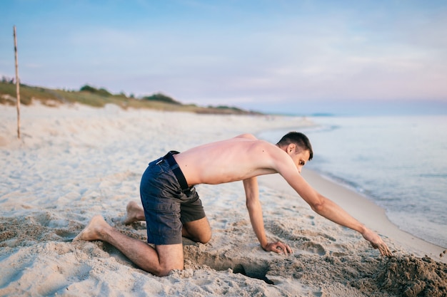 Homem na praia cavando um buraco na areia além do mar no verão