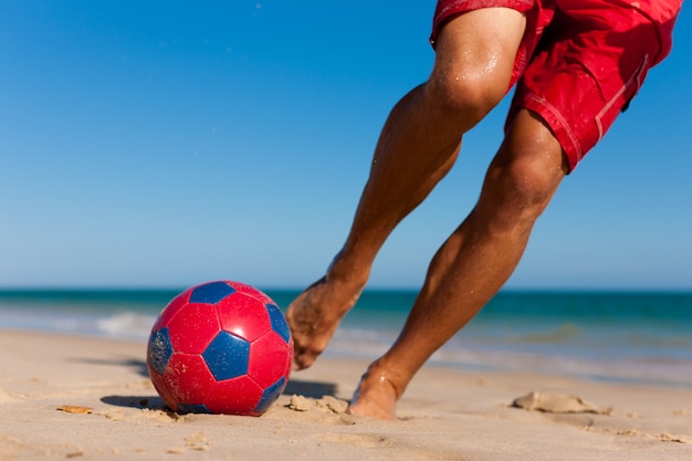 Homem na praia jogando futebol