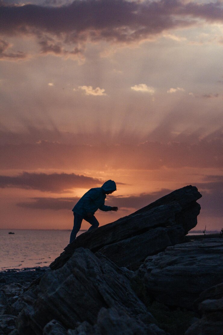 Foto homem na rocha ao lado do mar contra o céu durante o pôr do sol