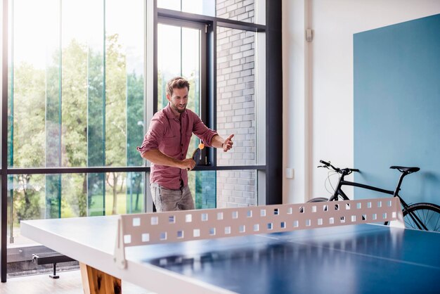 Homem na sala de descanso do escritório moderno jogando tênis de mesa