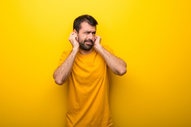 Homem nas orelhas amarelas vibrantes isoladas da coberta da cor com mãos. Expressão frustrada