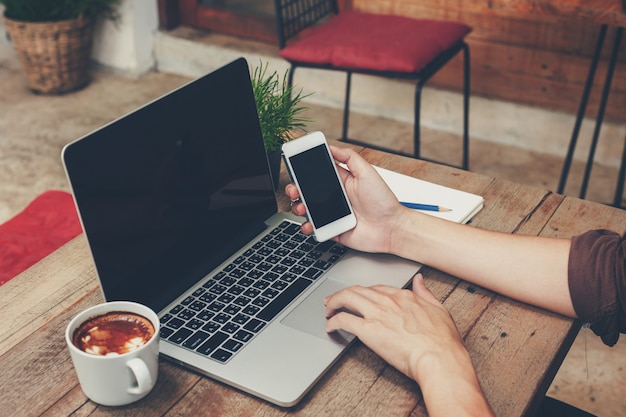 Homem negócio, segurando, telefone, e, usando computador portátil, ligado, tabela madeira