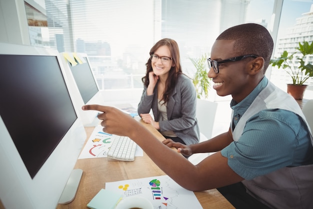 Homem negócios, apontar, computador, enquanto, sentando, com, coworker, escrivaninha, em, escritório