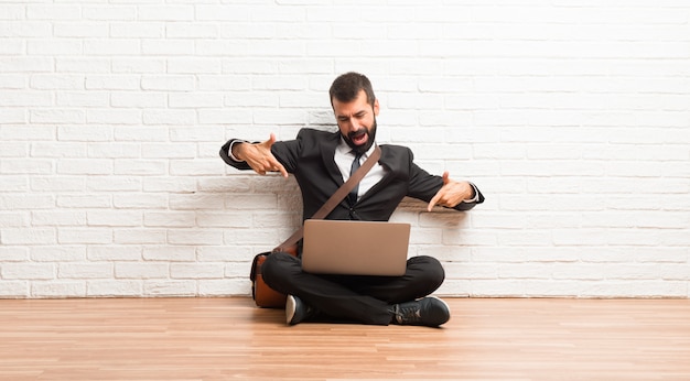 Homem negócios, com, seu, laptop, sentar chão, apontar, com, dedo, alguém, rir, muito