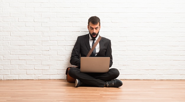 Homem negócios, com, seu, laptop, sentar chão, com, surpresa, e, choque, expressão facial