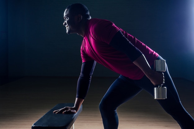 Homem negro afro-americano, atlético, correndo em esteiras, exercícios de alongamento nos grupos musculares, levantando-se da academia de bancada em fundo preto