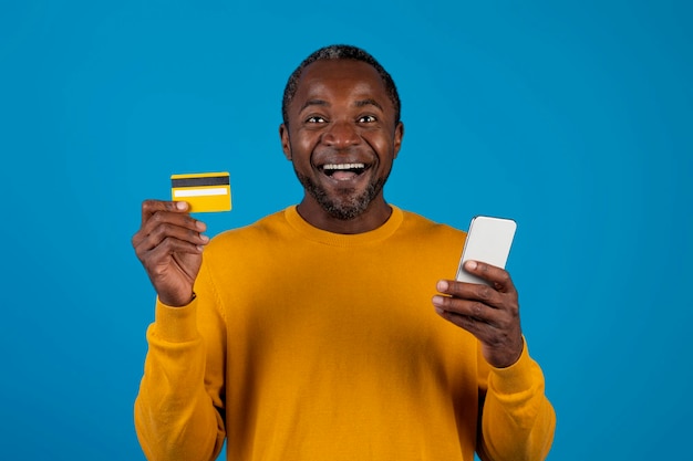 Homem negro animado segurando telefone celular e cartão de crédito