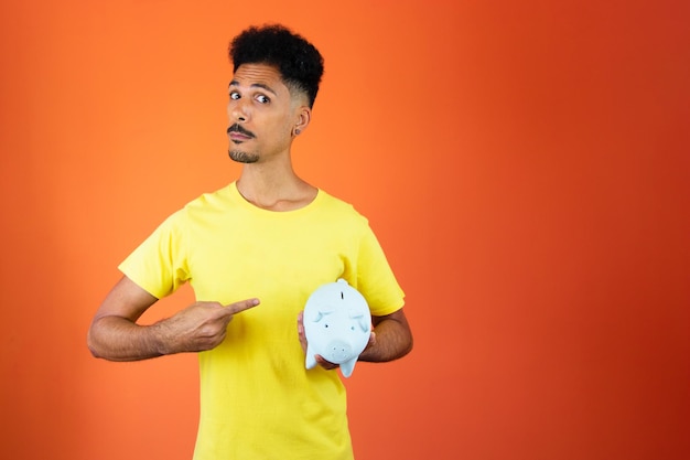 Homem negro bonito segurando um cofrinho isolado no homem laranja em uma camisa amarela isolada