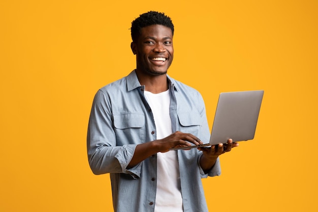 Homem negro bonito usando laptop moderno em amarelo