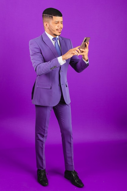 Homem negro brasileiro vestido de terno e homem de negócios de gravata violeta usando seu smartphone roxo