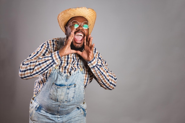 Homem negro brasileiro vestindo roupas country da festa junina festa de são joão arraia gritando promoção anunciando desconto de anúncio