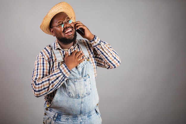 Homem negro brasileiro vestindo roupas country da festa junina festa de são joão arraia segurando a chamada de voz do smartphone