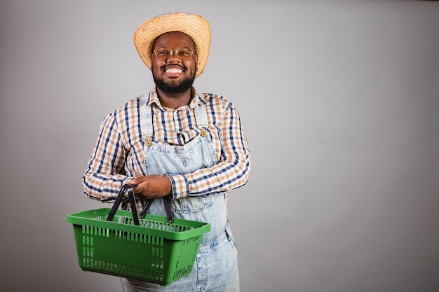 Homem negro brasileiro vestindo roupas country da festa junina festa de são joão arraia segurando promoções de compras de cesta de mercado