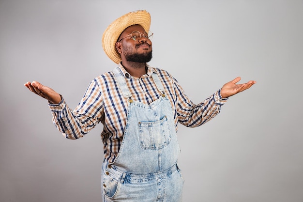 Homem negro brasileiro vestindo roupas country da festa junina festa de são joão com os braços abertos em dúvida