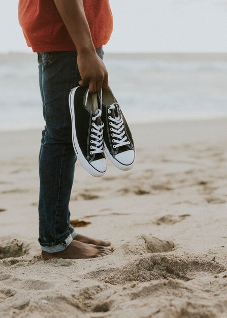 Homem negro carregando seus sapatos na praia