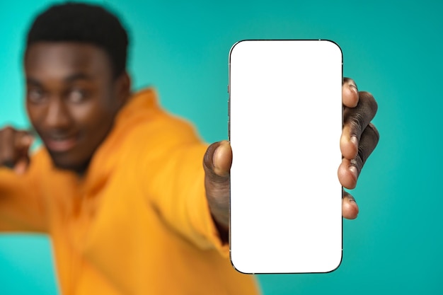 Homem negro casual sorridente apontando para a tela do celular branco em branco no estúdio