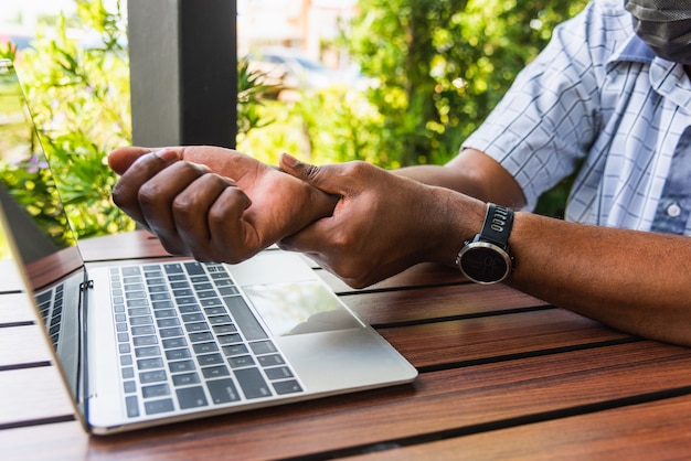 Homem negro com dor no pulso por usar um laptop