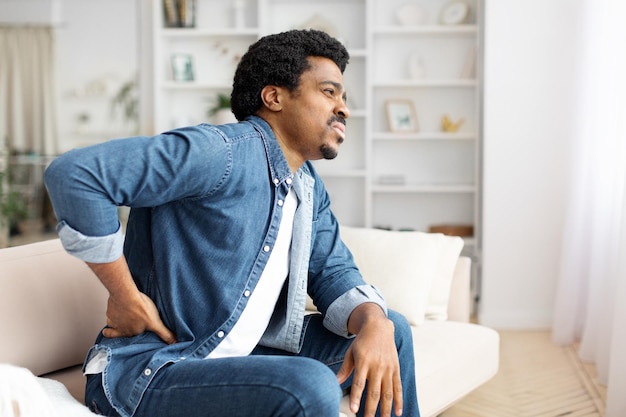 Homem negro com dores na parte inferior das costas em casa