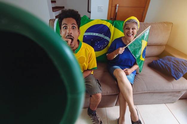 Foto homem negro de camisa amarela na sala assistindo tv torcendo pelo brasil