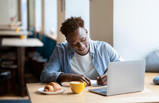 Homem negro feliz a estudar remotamente no portátil num café da cidade.