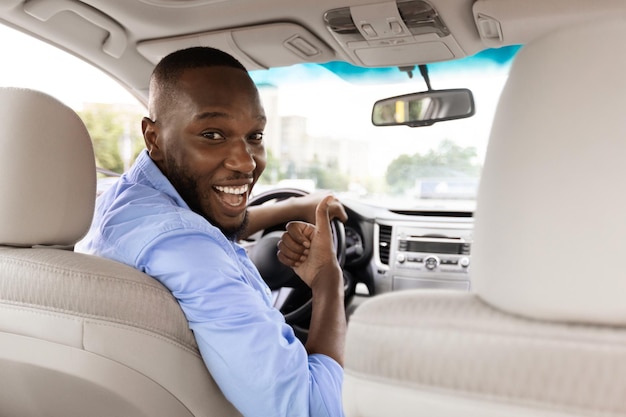 Homem negro feliz sentado no carro mostrando os polegares para cima gesto