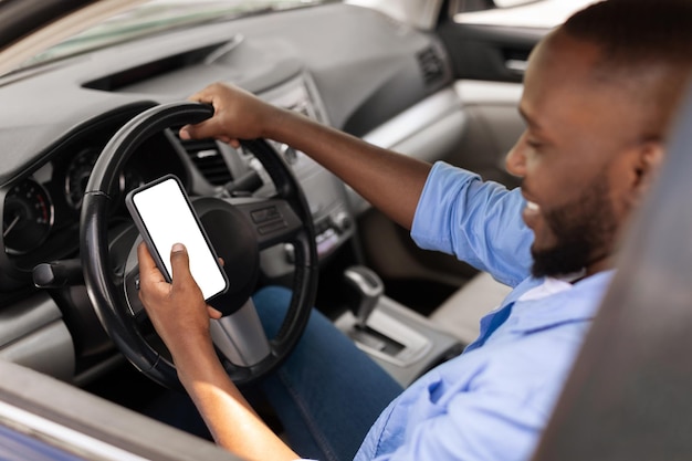 Homem negro feliz usando smartphone com tela vazia dirigindo carro