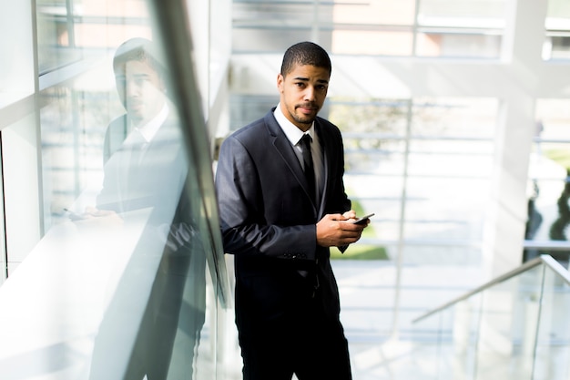Homem negro jovem bonito com telefone móvel no escritório