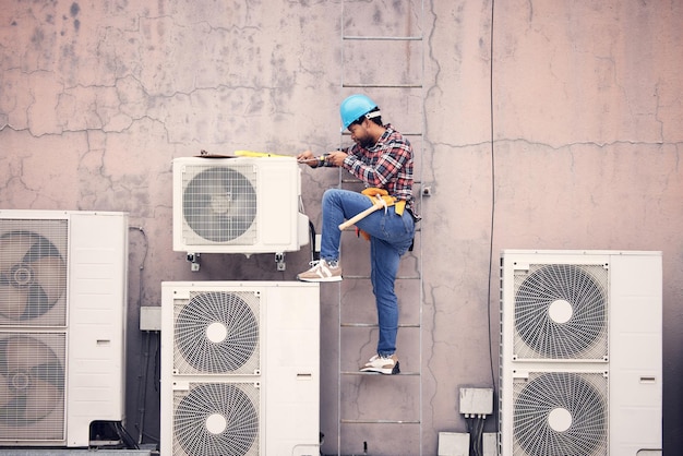 Homem negro reparo e manutenção técnica com engenharia e fixação de ar condicionado com ferramentas Serviço de faz-tudo e trabalho manual com tecnologia de eletricista masculino e capacete para segurança