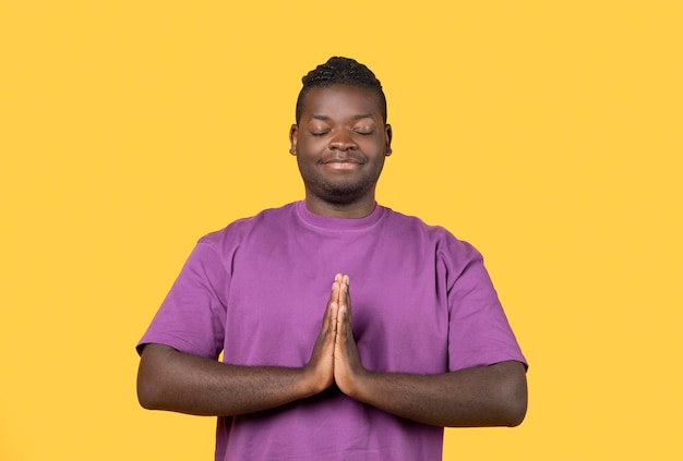 Homem negro rezando com os olhos fechados em pé sobre fundo amarelo