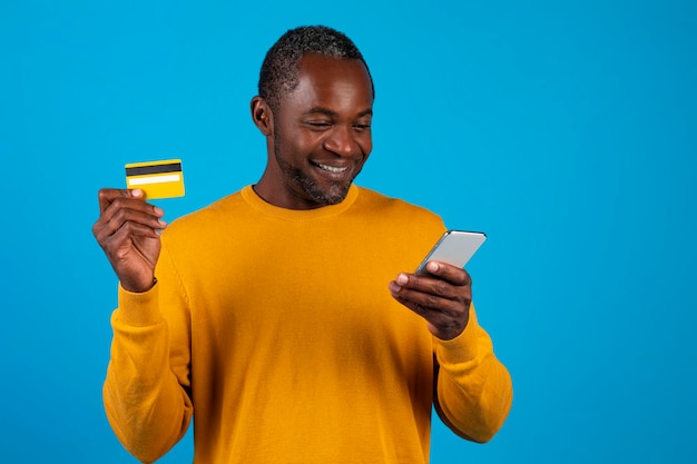 Homem negro sorridente segurando smartphone e cartão de crédito