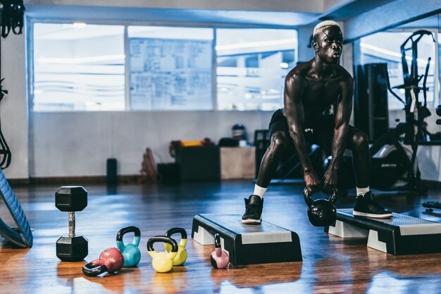 Foto homem negro treinando fitness com kettlebell dentro do clube de ginástica - foco no rosto