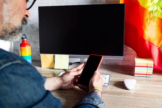 Homem no escritório com celular e acessórios LGBT e cultura LGBTQIA de bandeira gay