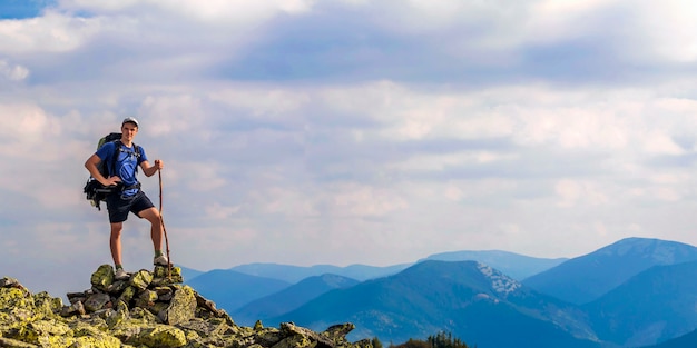 Homem no pico da montanha. Cena emocional. Jovem com mochila em pé com as mãos levantadas no topo de uma montanha e apreciando a vista para a montanha. Alpinista no topo da montanha. Esporte e vida ativa conceito.