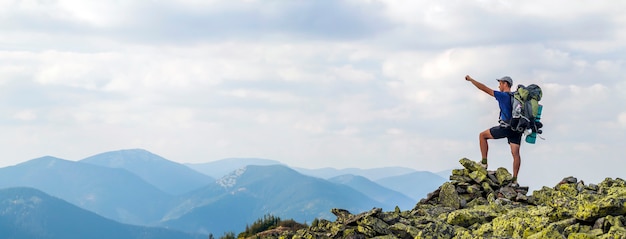 Homem no pico da montanha. cena emocional. jovem com mochila em pé com as mãos levantadas no topo de uma montanha e apreciando a vista para a montanha. alpinista no topo da montanha. esporte e vida ativa conceito.