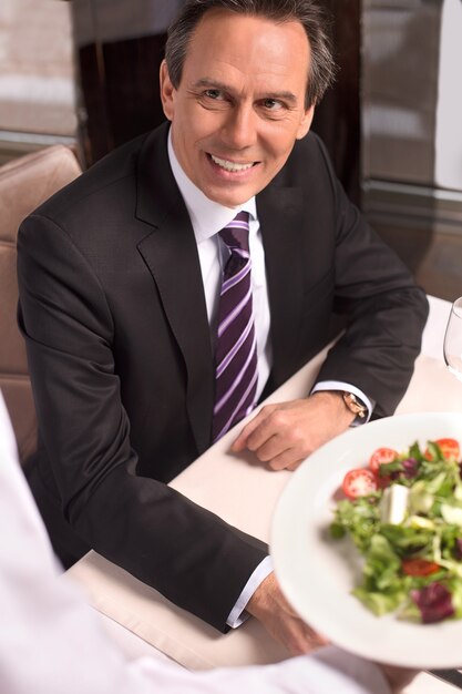 Foto homem no restaurante. vista superior do garçom segurando um prato com salada, enquanto o cliente olha para ele e sorri
