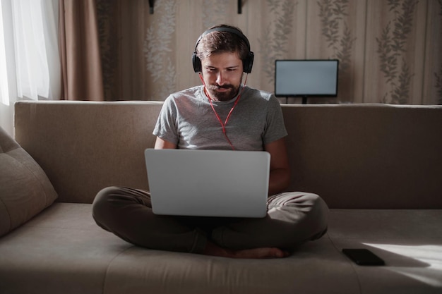 Homem no sofá com fones de ouvido e notebook em casa