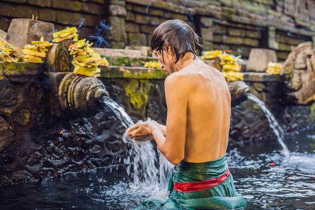 Homem no templo de água sagrada de nascente em bali. o complexo do templo consiste em uma petirtaan ou estrutura de banho, famosa por sua água sagrada.