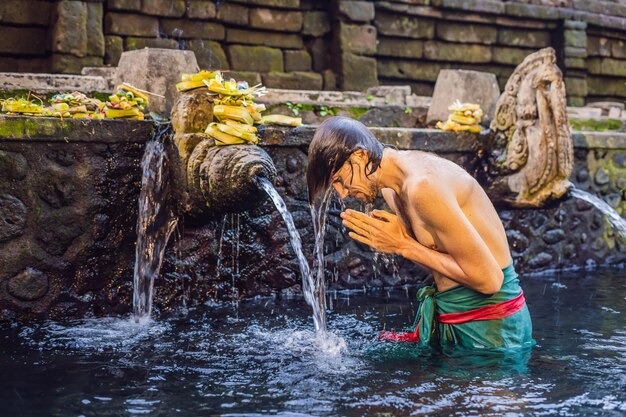 Foto homem no templo de água sagrada de nascente em bali. o complexo do templo consiste em uma petirtaan ou estrutura de banho, famosa por sua água sagrada.