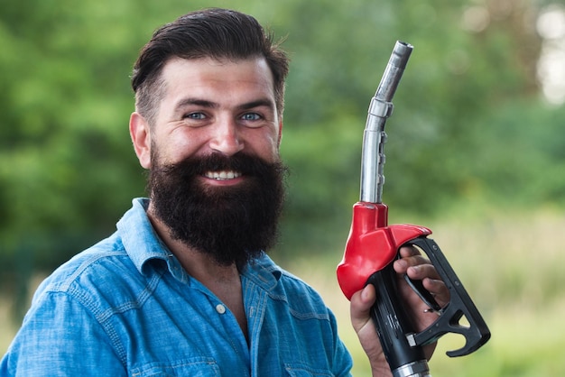 Homem nos bicos de enchimento da bomba de gasolina Posto de gasolina Retrato de homem barbudo segurar o bico de abastecimento de gasolina bomba de combustível