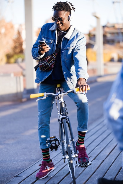 Homem novo bonito que usa o telefone móvel e a bicicleta ajustada da engrenagem na rua.