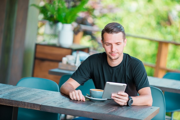 Homem novo com o portátil no café bebendo do café ao ar livre. Homem usando smartphone móvel.