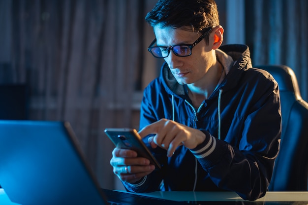 Homem novo com vidros que trabalha em um portátil na noite. Freelancer está trabalhando até tarde em um projeto em casa.